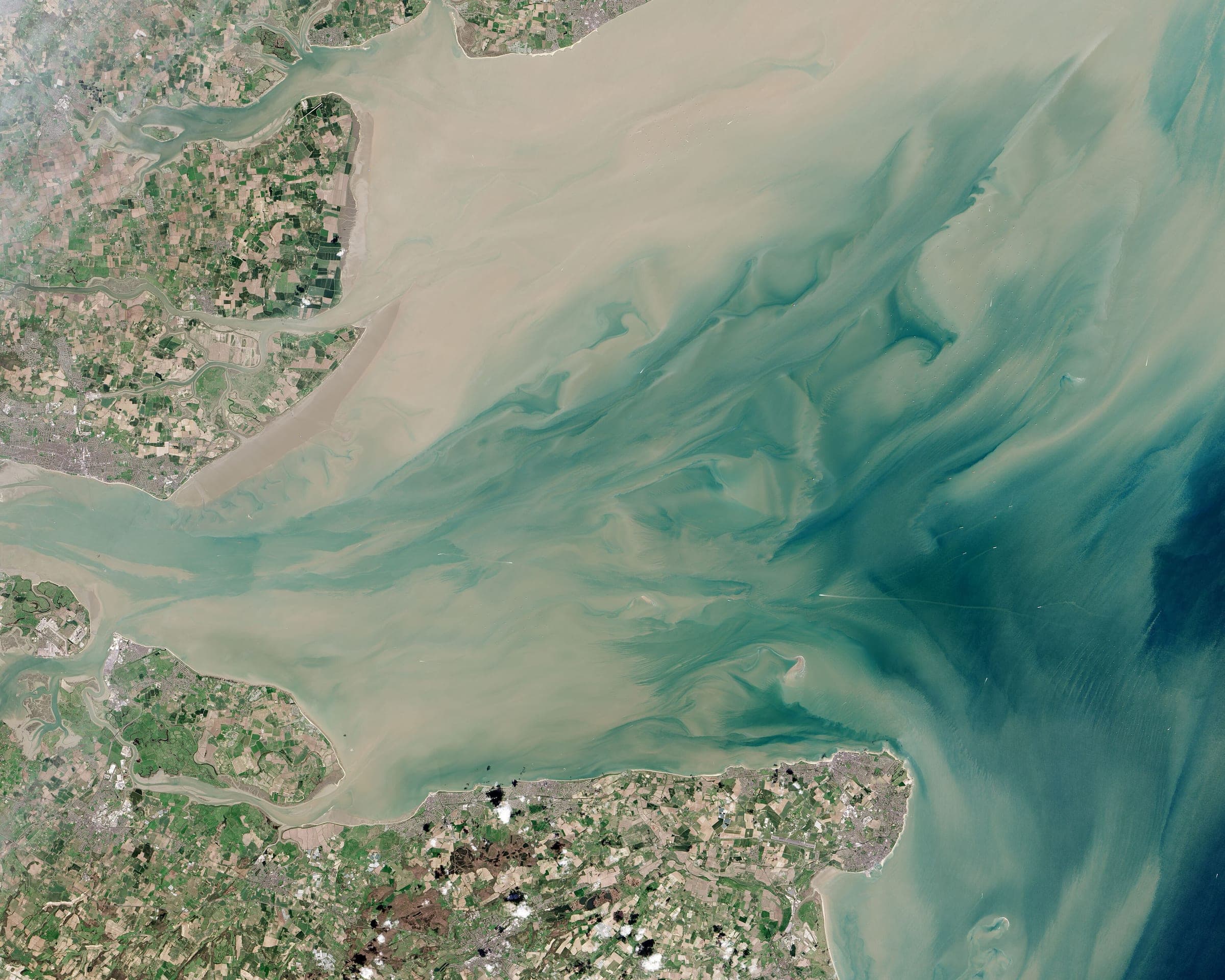 The Thames estuary opening into the North Sea, sediment plumes fanning off the Essex and Kent shores. Landsat frame, 30 metres per pixel.