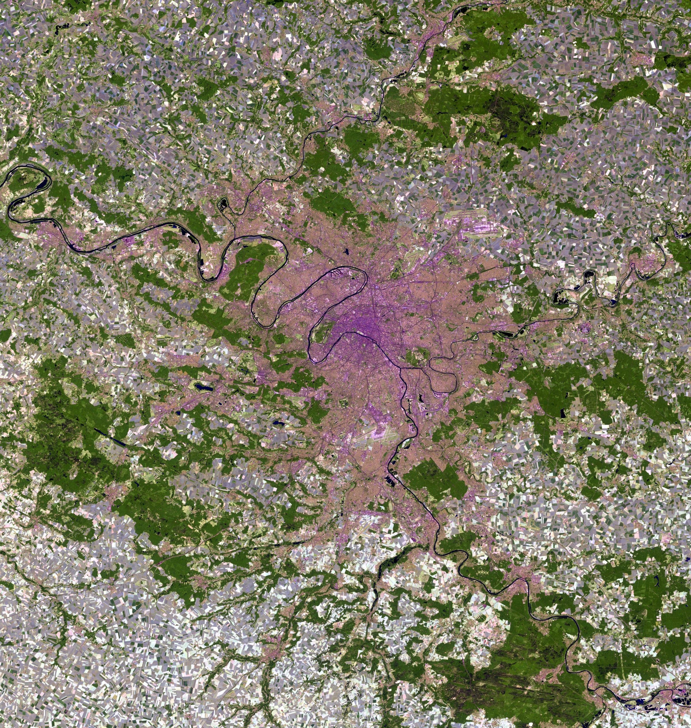 Paris in false colour, the band assignment that returns living vegetation as red: the Bois de Boulogne and the Bois de Vincennes read as two dark lobes on either side of the city. Landsat frame, 30 metres per pixel.